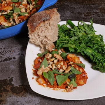 Romesco beans on a plate, with broccoli rabe, and bread. Pan in upper left corner.