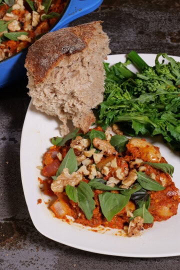 Romesco beans on a plate, with broccoli rabe, and bread. Pan in upper left corner.