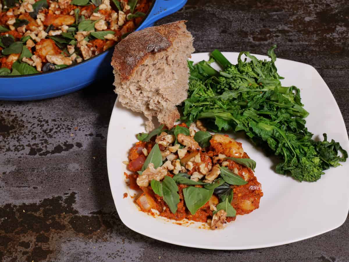 Romesco beans on a plate, with broccoli rabe, and bread. Pan in upper left corner.